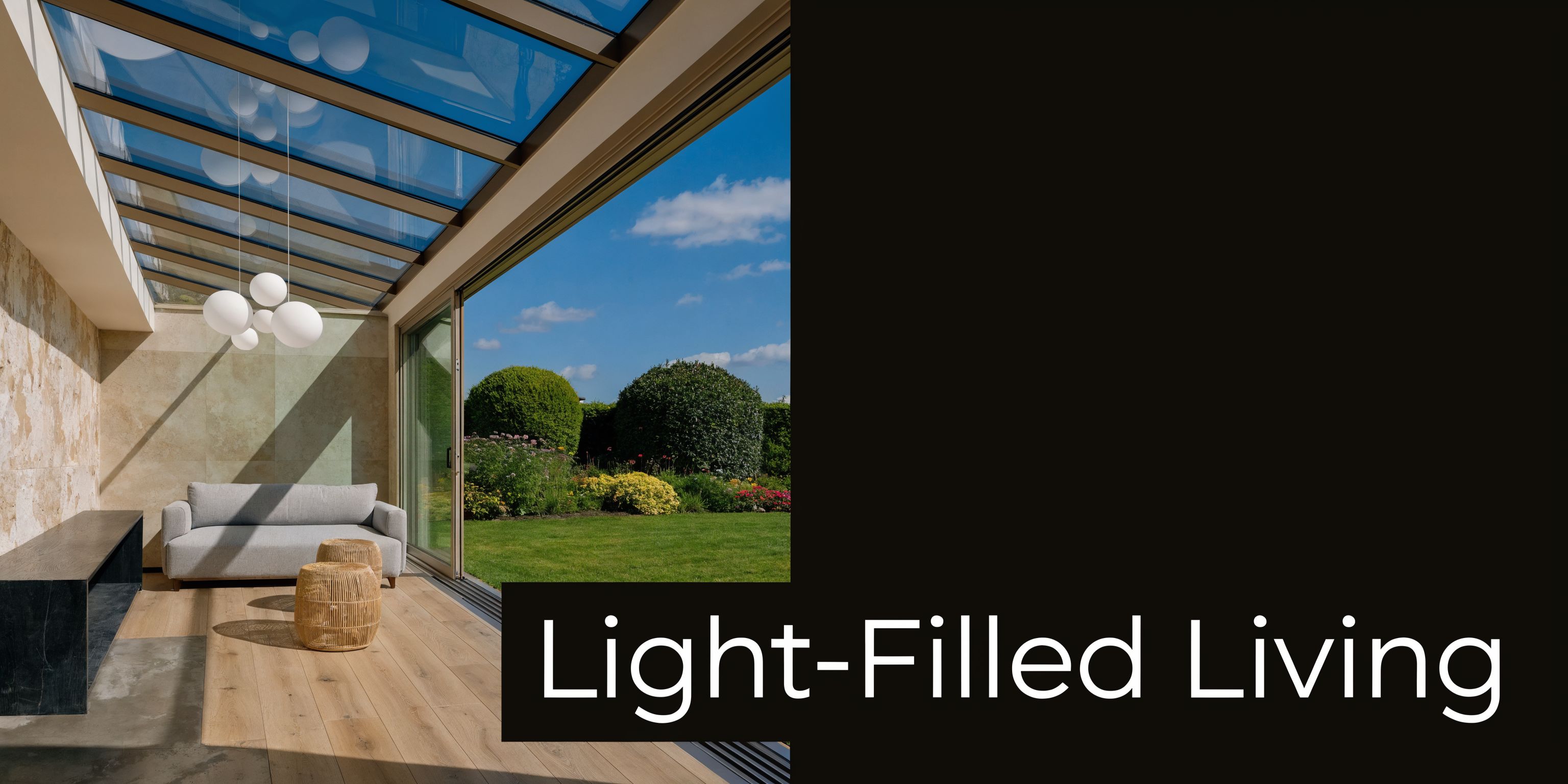 A modern sunroom with a glass roof extension, wooden flooring, and a view of a lush garden.