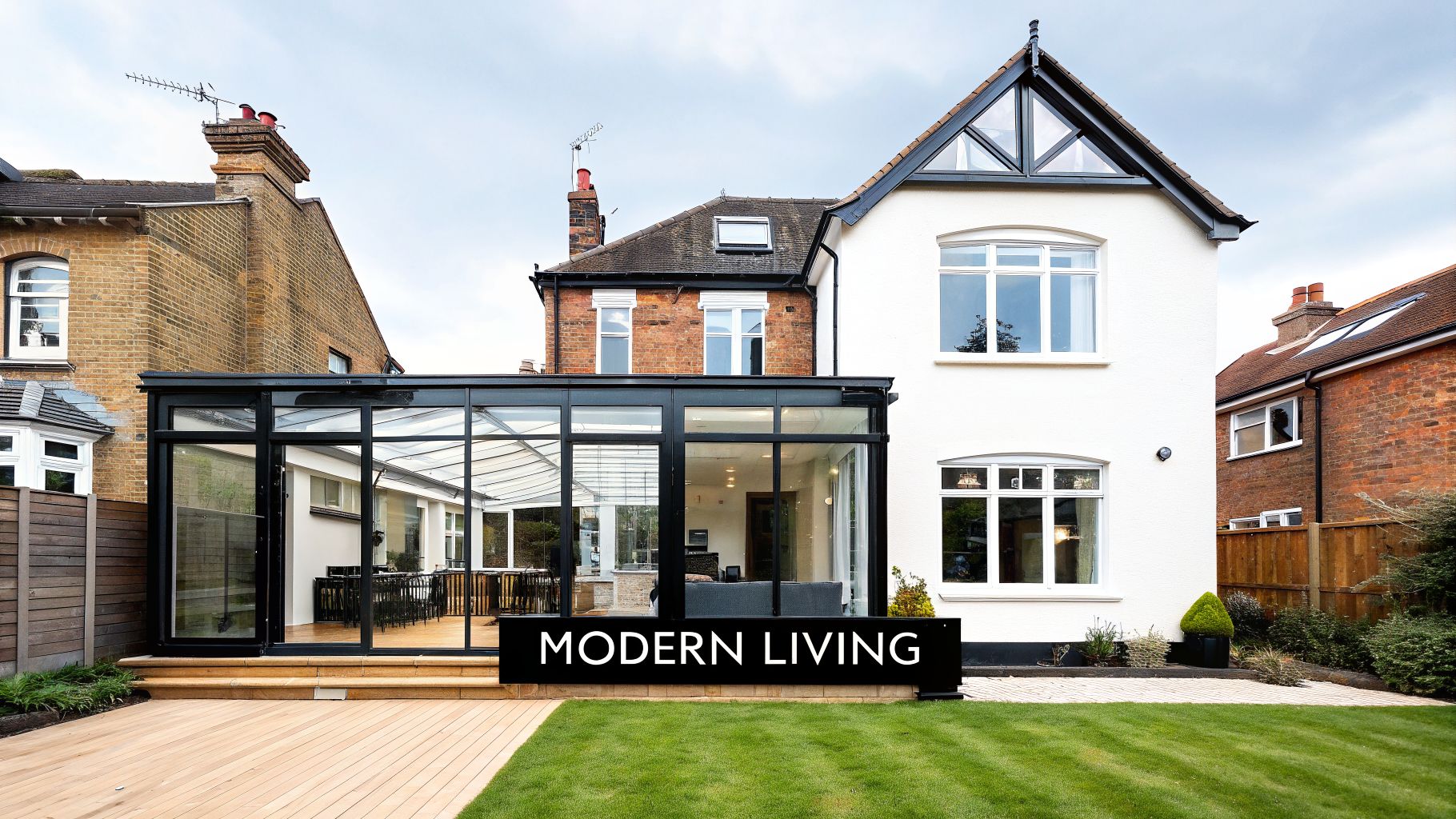 A modern glass conservatory extension on a traditional white house with a vibrant green lawn.