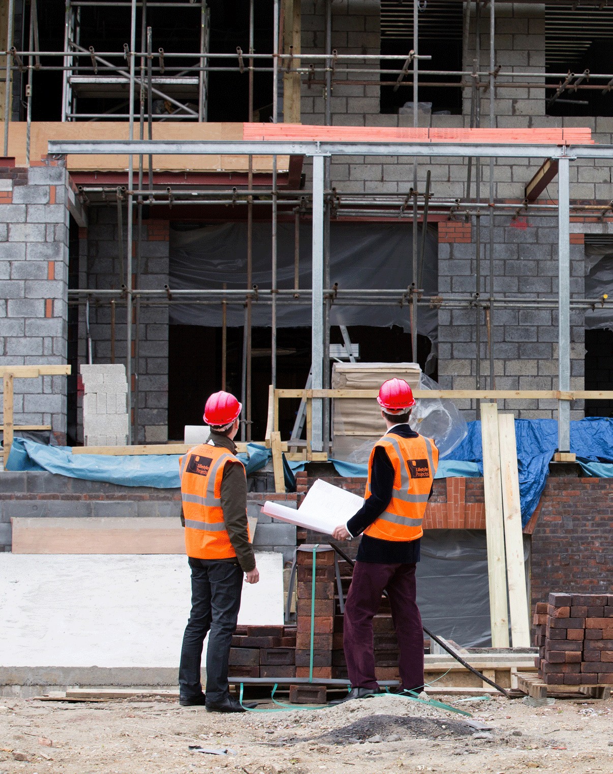 Two people in red hard hats and hi-vis vests reviewing drawings on a construction site