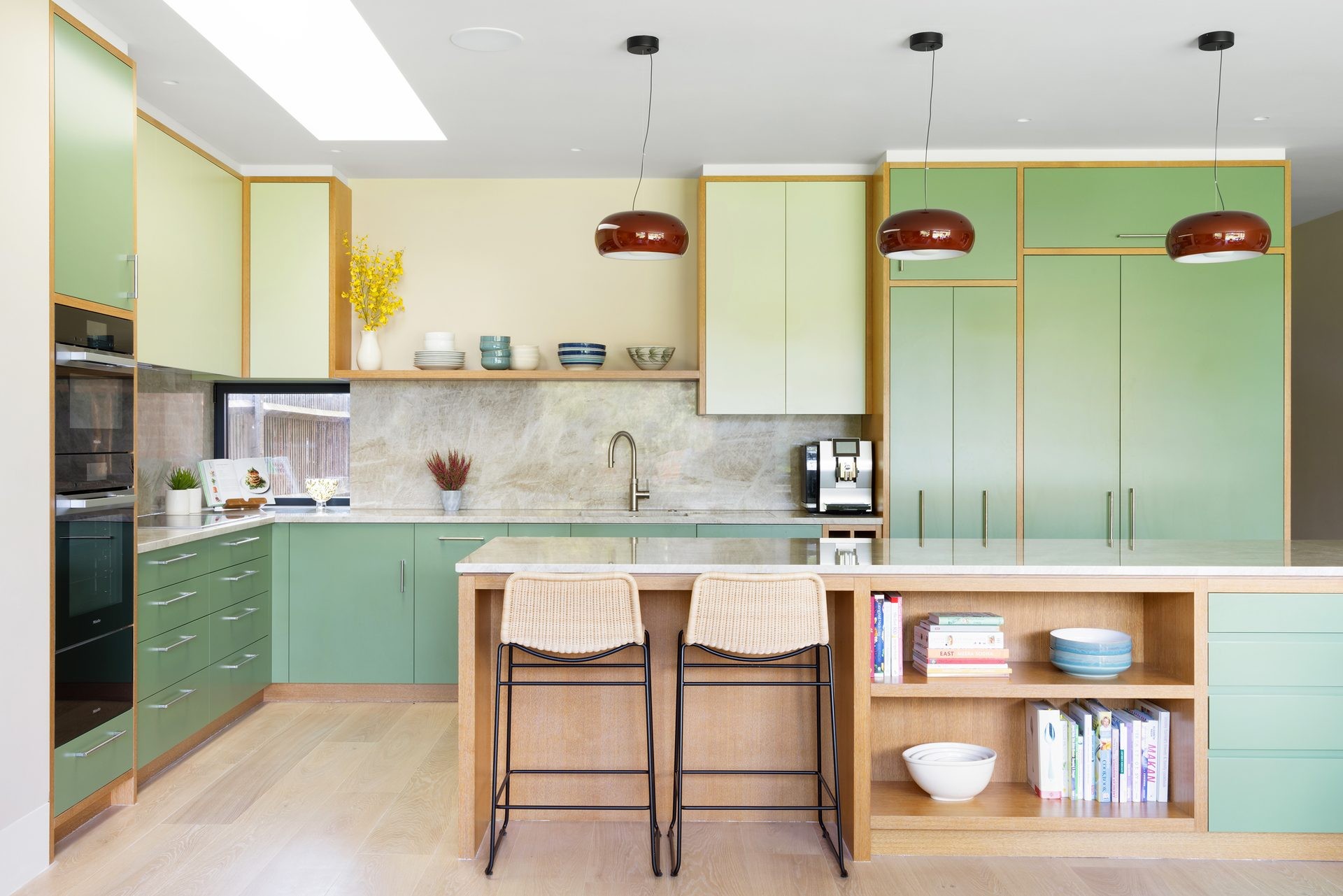 Pale green kitchen with a central island, oak shelving and pendant lights