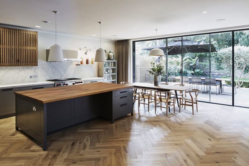 Open-plan kitchen with herringbone floor and full-height glazing onto the garden